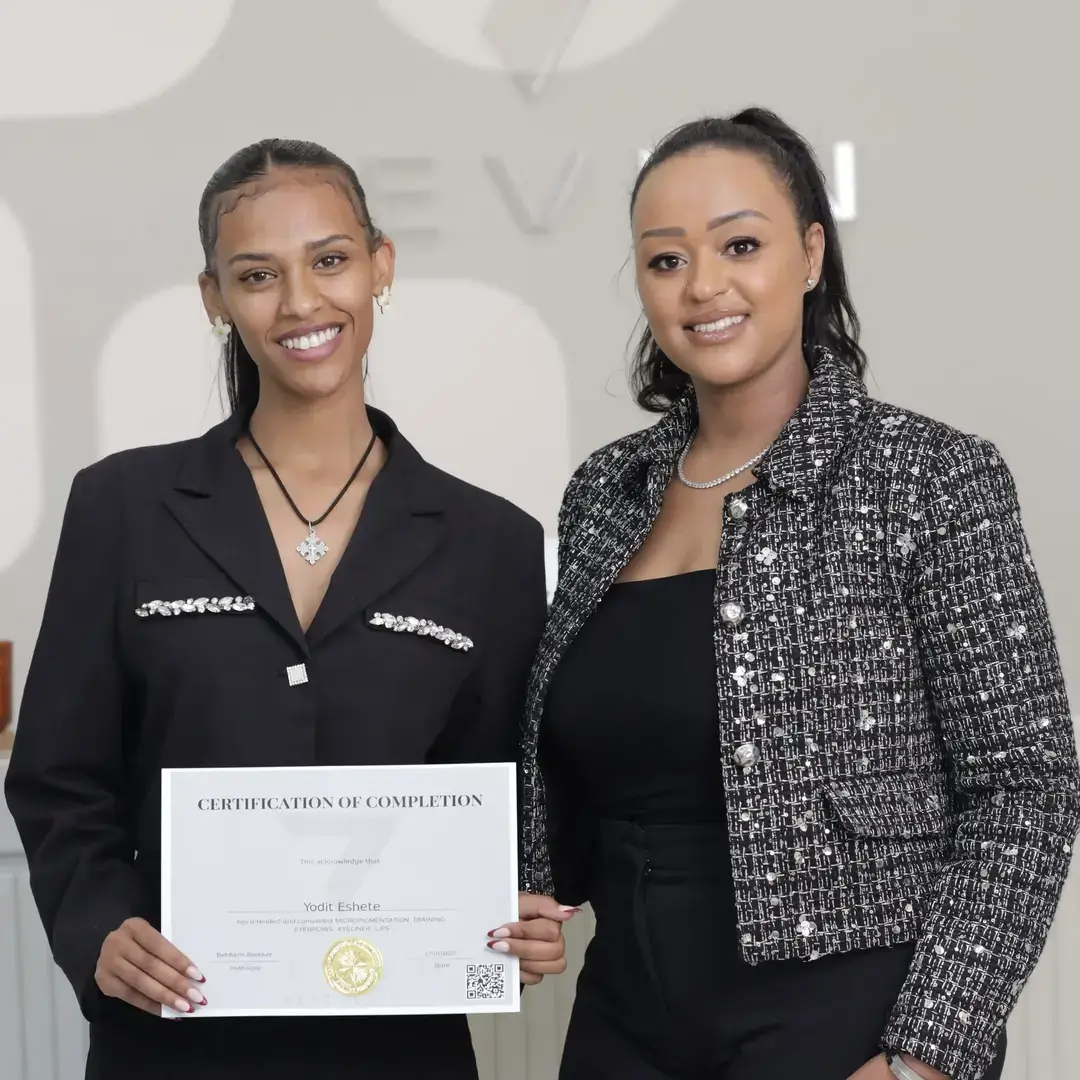Permanent Makeup Certification at Seven Aesthetics: Teacher Betlehem Bereket with student Solomon Birhanu holding his certificate of completion, celebrating with champagne after completing the course.