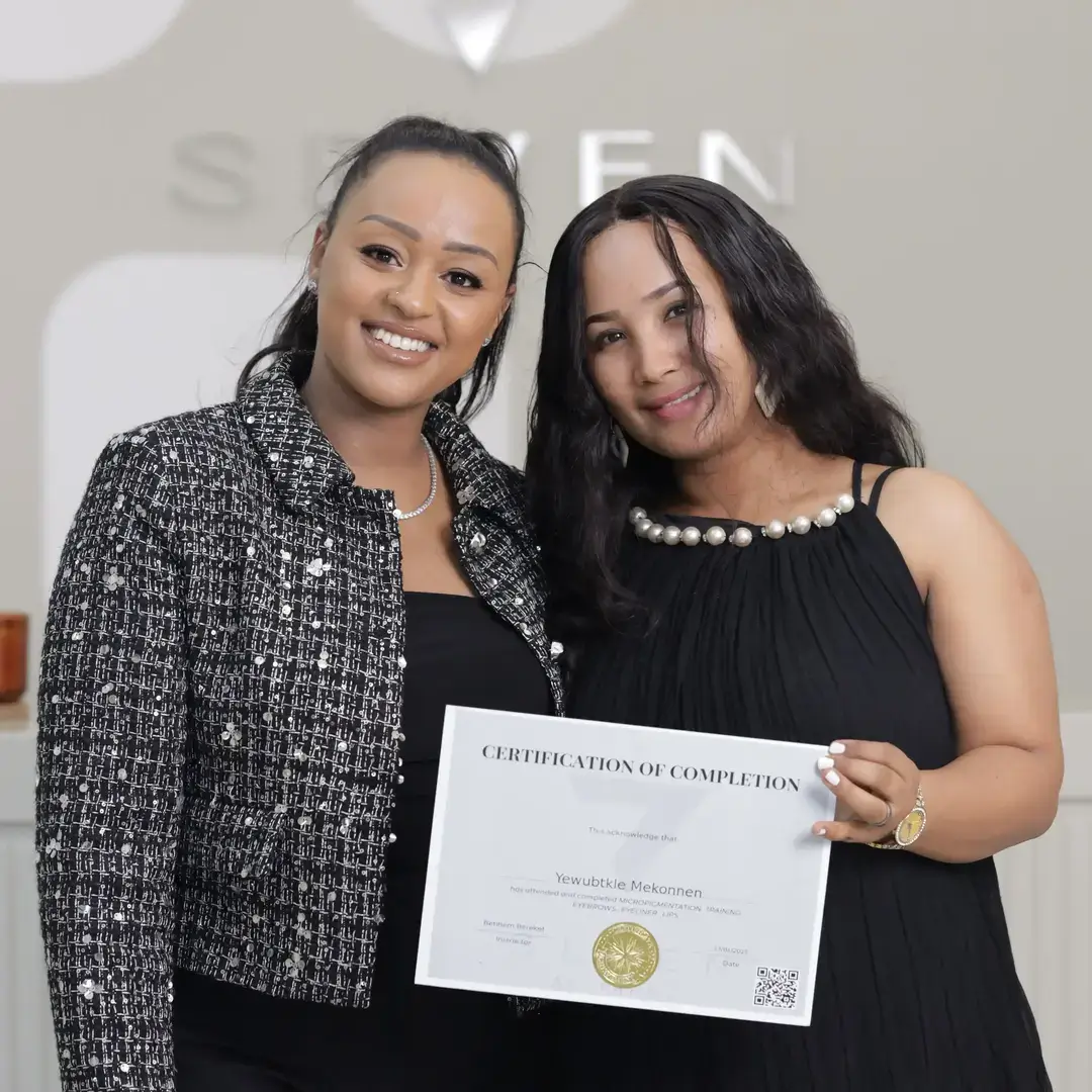 Permanent Makeup Certification at Seven Aesthetics: Teacher Betlehem Bereket with student Awraris Melesse holding his certificate of completion after completing the course.